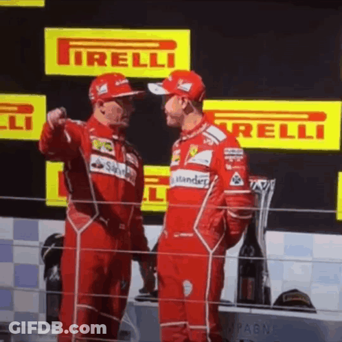 Two Men In Red Ferrari Uniforms Are Standing Next To Each Other On A Podium GIF