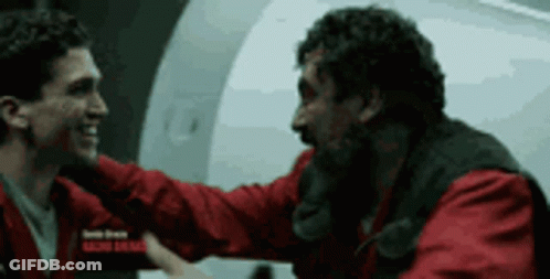 Two Men In Red Jackets Are Hugging Each Other In Front Of A White Wall . GIF