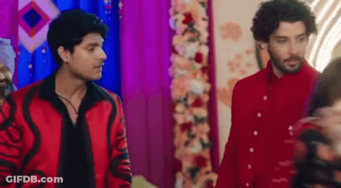Two Men In Red Jackets Near Flower Arrangement GIF