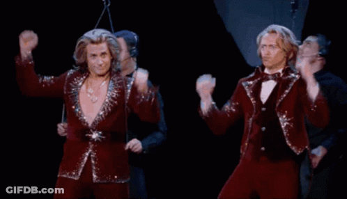 Two Men In Red Suits Are Dancing On A Stage With Their Arms In The Air GIF