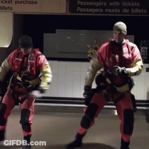 Two Men In Safety Suits Are Dancing In Front Of A Sign That Says Passengers With Tickets GIF