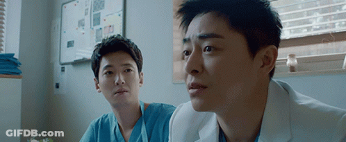 Two Men In Scrubs Are Sitting In A Room And Looking At Something . GIF