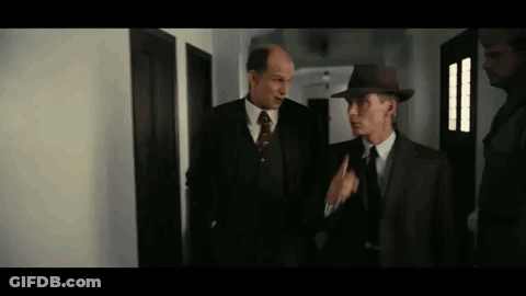 Two Men In Suits And Hats Are Standing Next To Each Other In A Hallway Talking To Each Other . GIF