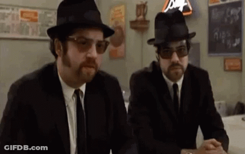 Two Men In Suits And Hats At Table GIF