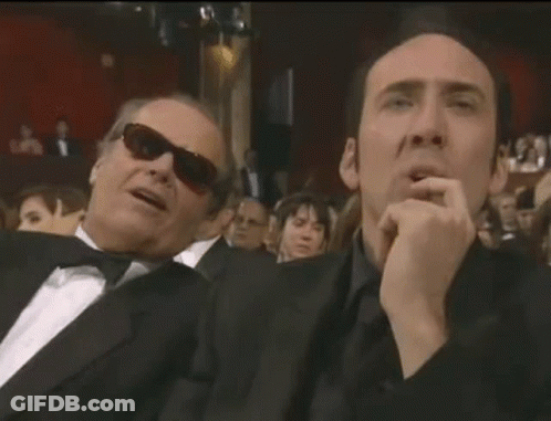 Two Men In Suits And Sunglasses Are Sitting Next To Each Other In A Crowd . GIF