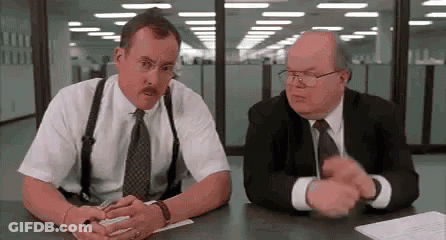 Two Men In Suits And Suspenders Are Sitting At A Table Talking To Each Other . GIF