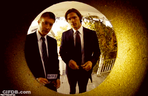 Two Men In Suits And Ties Are Looking Through A Hole In A Wall That Says Praytocastici GIF