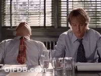 Two Men In Suits And Ties Are Sitting At A Table With Glasses Of Water And Papers . GIF