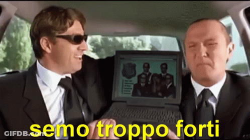 Two Men In Suits And Ties Are Sitting In A Car And One Is Holding A Laptop With A Picture Of A Group Of Men On It GIF