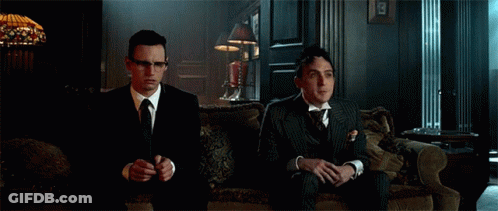 Two Men In Suits And Ties Are Sitting On A Couch And Clapping Their Hands . GIF