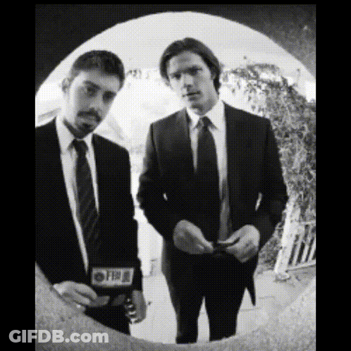 Two Men In Suits And Ties Are Standing Next To Each Other And One Of Them Has A Cbs Sticker On His Jacket GIF