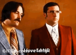 Two Men In Suits And Ties Are Standing Next To Each Other And One Of Them Is Saying `` I Loveland '' . GIF
