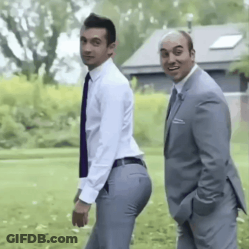 Two Men In Suits And Ties Are Standing Next To Each Other In A Grassy Field . GIF