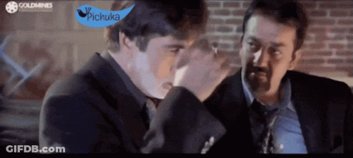Two Men In Suits And Ties Are Talking In Front Of A Brick Wall With A Blue Sign That Says Pichuka GIF