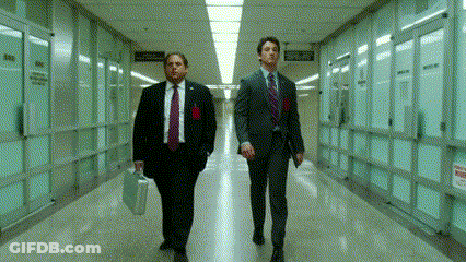Two Men In Suits And Ties Are Walking Down A Hallway With A Sign On The Wall That Says " No Smoking " GIF