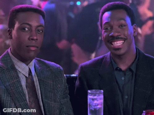 Two Men In Suits And Ties Sitting At Table With Drinks GIF