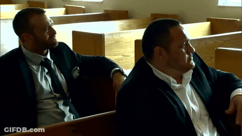 Two Men In Suits Are Sitting In A Church Talking GIF