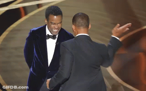 Two Men In Suits Are Standing Next To Each Other On A Stage And Shaking Hands . GIF