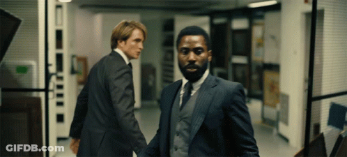 Two Men In Suits Are Walking Down A Hallway And One Has A Beard GIF