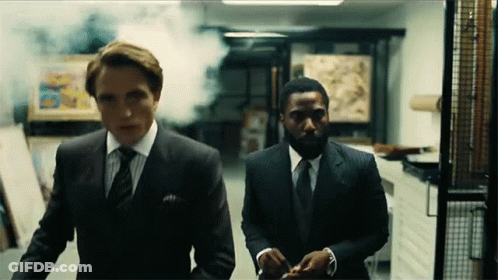 Two Men In Suits Are Walking Down A Hallway With Smoke Coming Out Of It . GIF