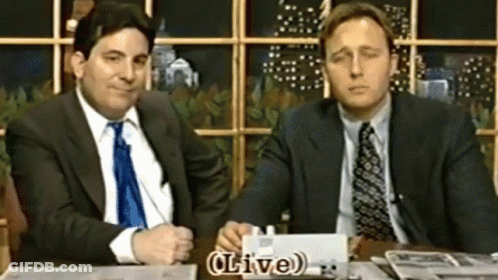 Two Men In Suits At Table With Live Sign GIF