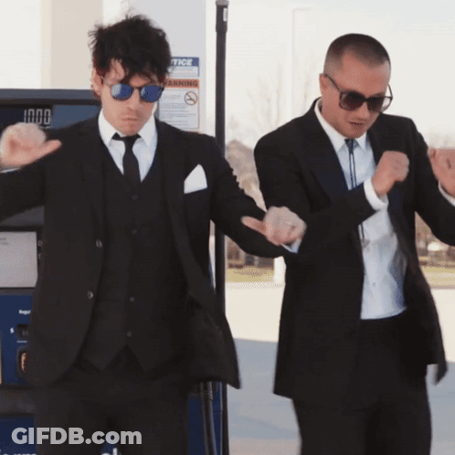 Two Men In Suits Dancing In Front Of A Gas Pump That Says Notice On It GIF