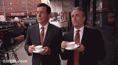 Two Men In Suits Holding Coffee On City Street GIF