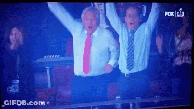 Two Men In Suits Raising Arms In Front Of Fox 11 Screen GIF