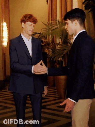Two Men In Suits Shake Hands Near Plant GIF