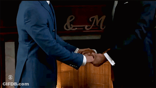 Two Men In Suits Shaking Hands In Front Of Fireplace With Sign & N GIF