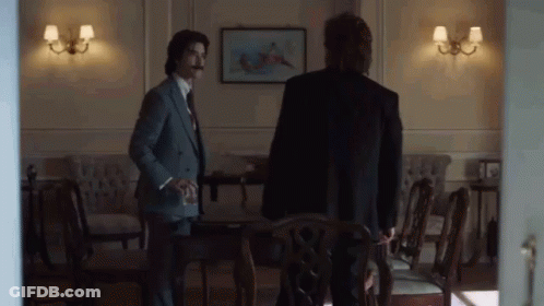 Two Men In Suits Standing In Room With Chairs GIF