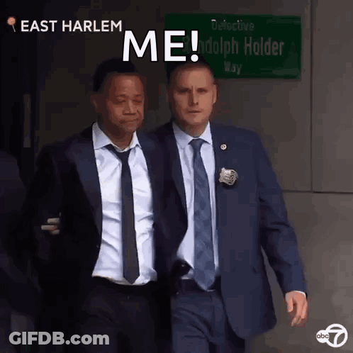Two Men In Suits Walking Past East Harlem Sign GIF