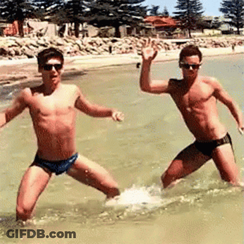 Two Men In Swim Trunks Are Standing In The Water . GIF