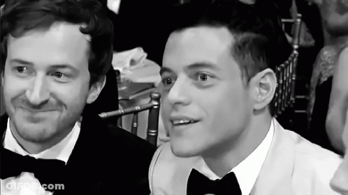 Two Men In Tuxedos And Bow Ties Are Sitting Next To Each Other At A Table . GIF