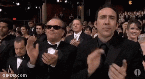 Two Men In Tuxedos And Sunglasses Are Clapping In A Crowd Of People . GIF