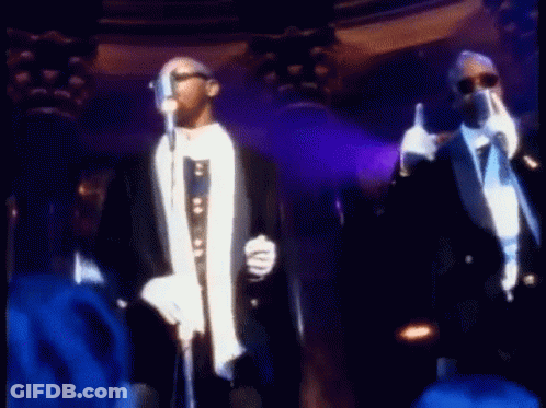 Two Men In Tuxedos Are Singing Into Microphones On Stage . GIF