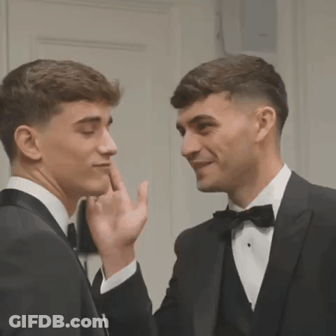 Two Men In Tuxedos Are Standing Next To Each Other And Touching Their Faces . GIF