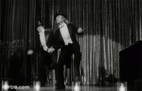 Two Men In Tuxedos Dancing On Stage GIF