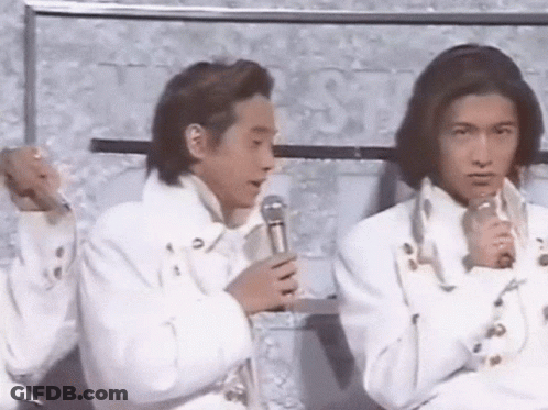 Two Men In White Jackets Are Sitting Next To Each Other And Holding Microphones . GIF