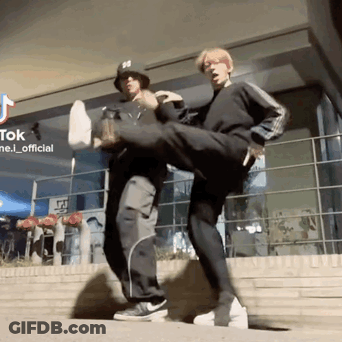 Two Men Kicking Each Other In Front Of Tik Tok Building GIF