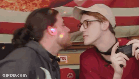 Two Men Kissing Under American Flag, One Wearing Glasses GIF