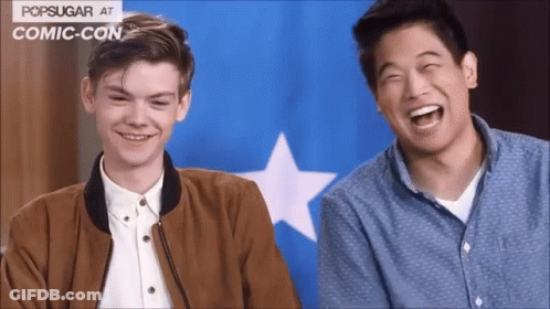 Two Men Laughing In Front Of Blue And White Popsugar Flag At Comic Con GIF