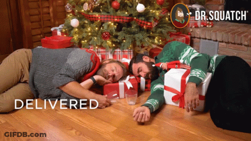 Two Men Laying In Front Of Christmas Tree Dr. Squatch GIF