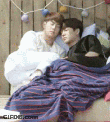 Two Men Laying On Bed With Striped Blanket GIF