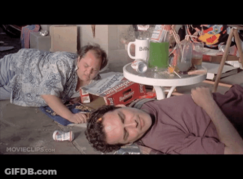 Two Men Laying On The Ground In Front Of A Table With A Mug That Says Billy GIF