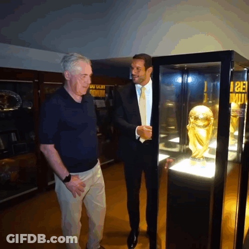 Two Men Looking At Trophy With Stadium Sign GIF