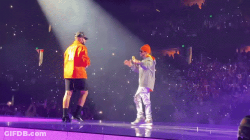 Two Men On A Stage With One Wearing An Orange Jacket With The Number 12 On It GIF