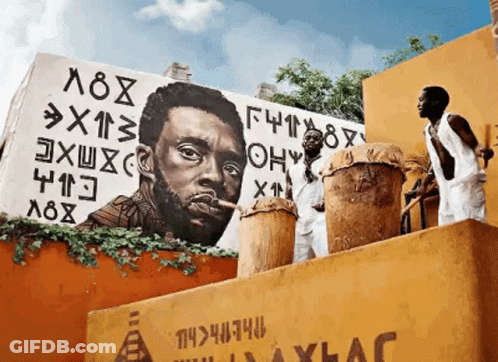 Two Men Playing Drums In Front Of A Mural Of A Man With A Cigar GIF