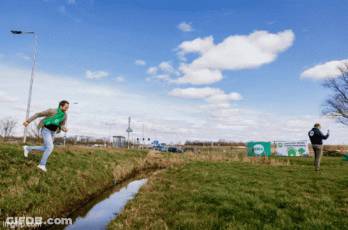 Two Men Playing Frisbee In Field With Recycling Sign GIF