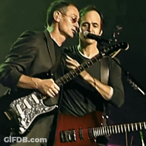 Two Men Playing Guitars And Singing Into Microphones GIF